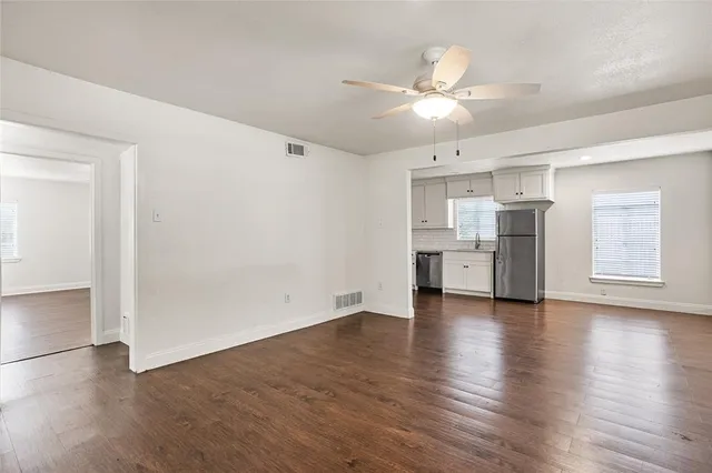 an empty room with wooden floor cabinet and a kitchen view
