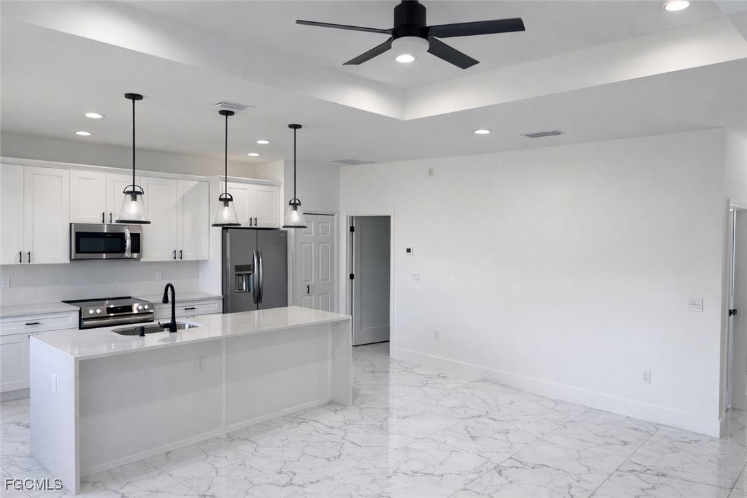 3903 11th Street Southwest Lehigh Acres, FL 33976 - Photo 4 of 12 a large kitchen with stainless steel appliances kitchen island granite countertop a refrigerator a stove a oven and white cabinets with wooden floor