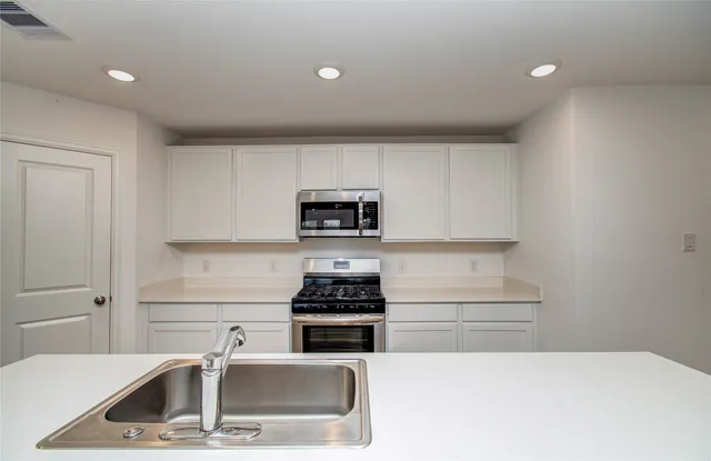 a kitchen with stainless steel appliances a stove a sink and white cabinets