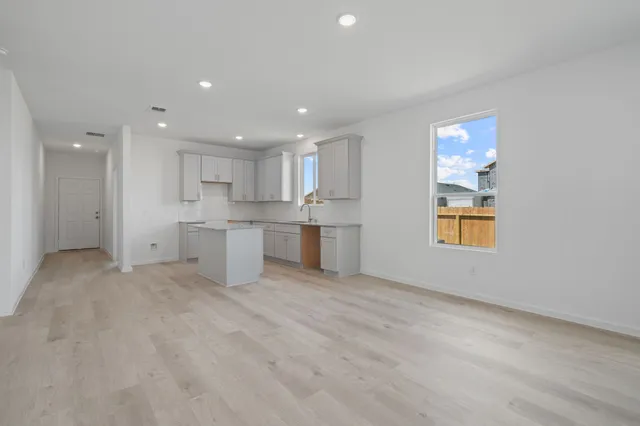 a view of an empty room with kitchen and window