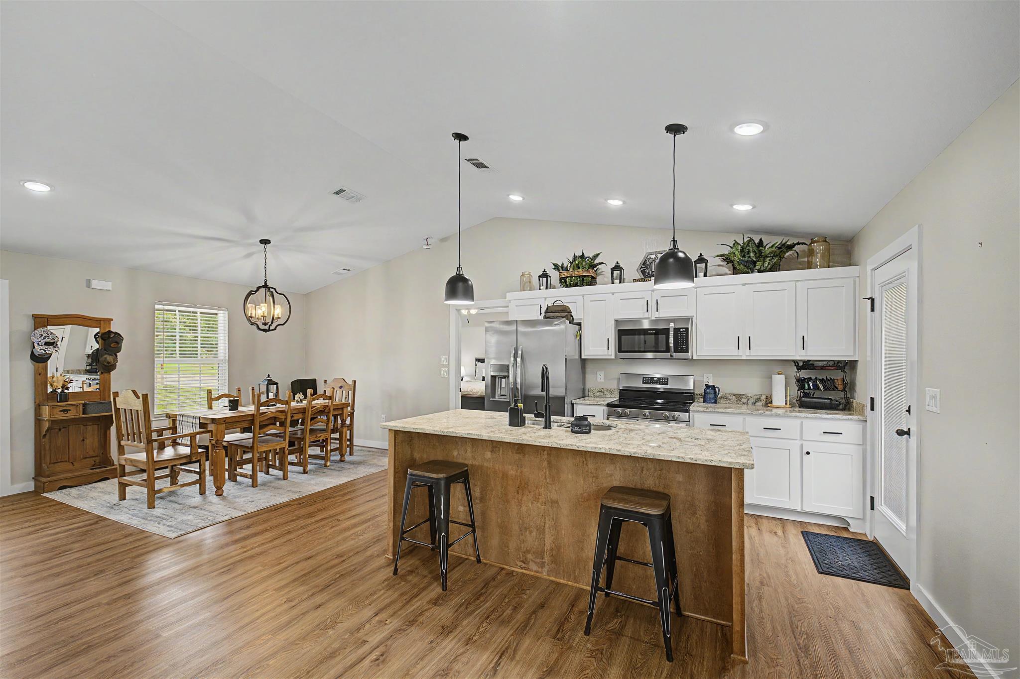 2549 Ten Mile Road Pace, FL 32571 - Photo 19 of 46 a kitchen with stainless steel appliances kitchen island granite countertop a stove a refrigerator a kitchen island a dining table and chairs with wooden floor
