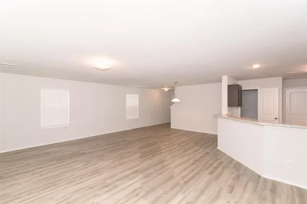 an empty room with wooden floor and kitchen view