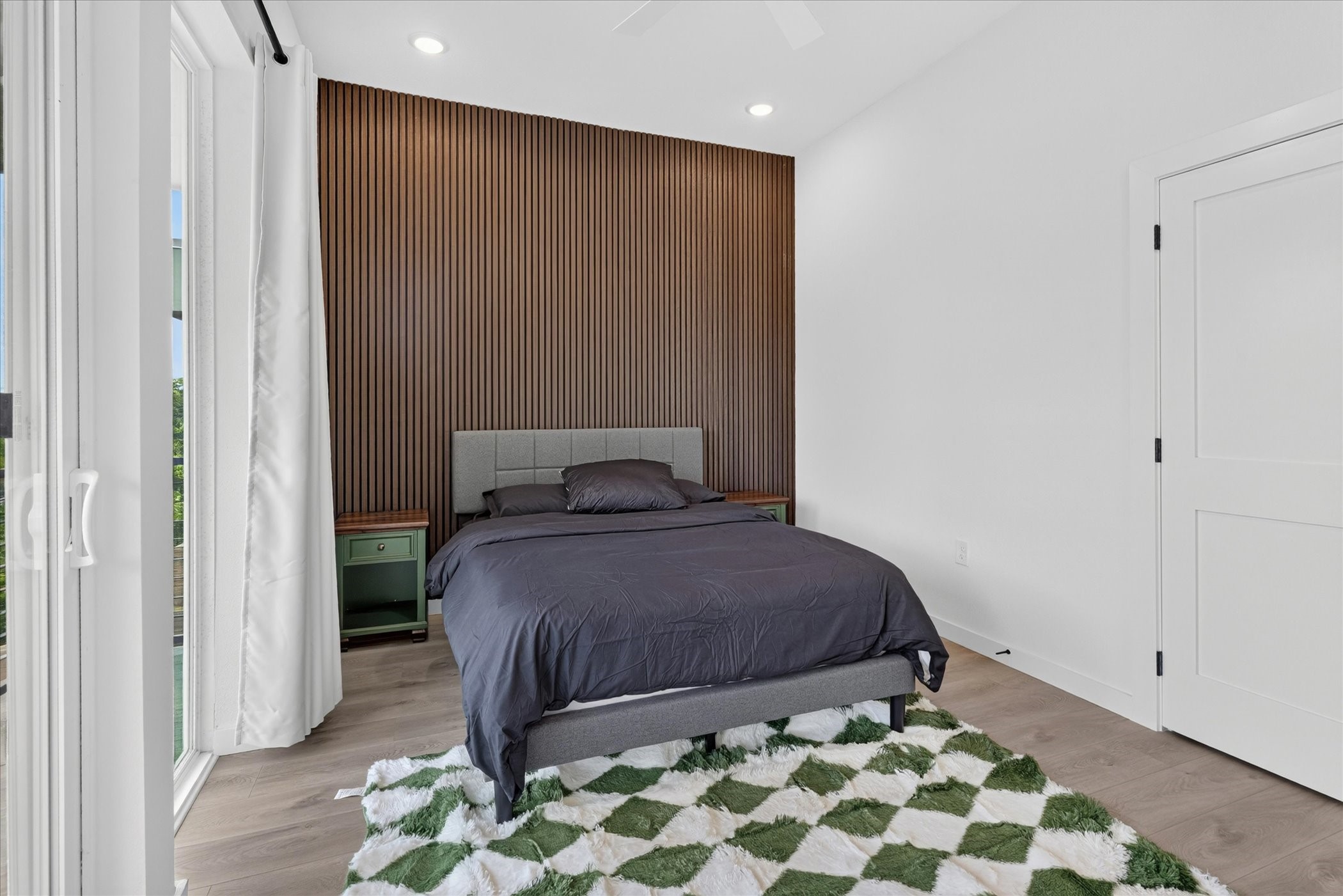 2000 Riverside Farms Road, Unit 8101 Austin, TX 78741 - Photo 21 of 41 This bedroom features a modern design with a textured accent wall, a cozy bed, and sliding glass doors that let in ample natural light. The space is bright and inviting, complemented by a stylish rug and neutral tones.