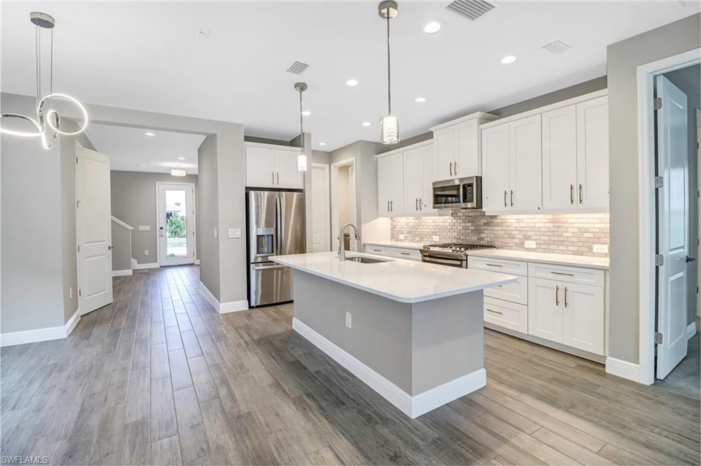4652 Centaurus Circle Naples, FL 34120 - Photo 5 of 45 Kitchen featuring stainless steel appliances, white cabinets, a kitchen island with sink, backsplash, and light stone countertops