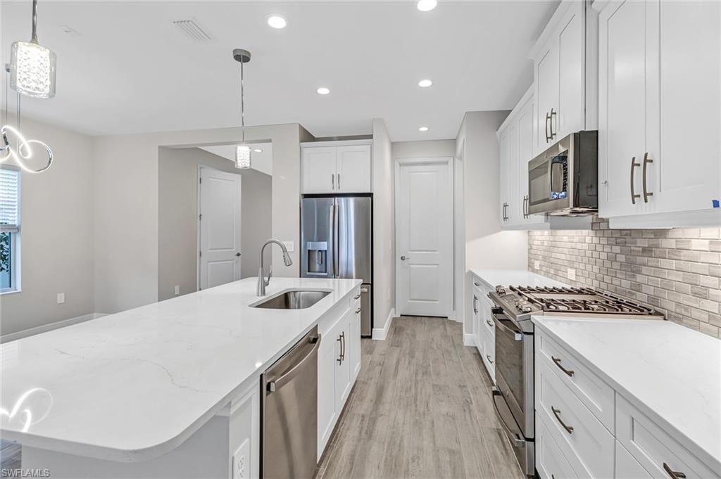 4652 Centaurus Circle Naples, FL 34120 - Photo 6 of 45 Kitchen with stainless steel appliances, a center island with sink, light stone counters, light wood-type flooring, and white cabinetry