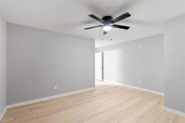 a view of an empty room with wooden floor and a ceiling fan