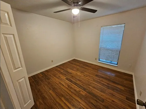 a view of an empty room with wooden floor and a ceiling fan
