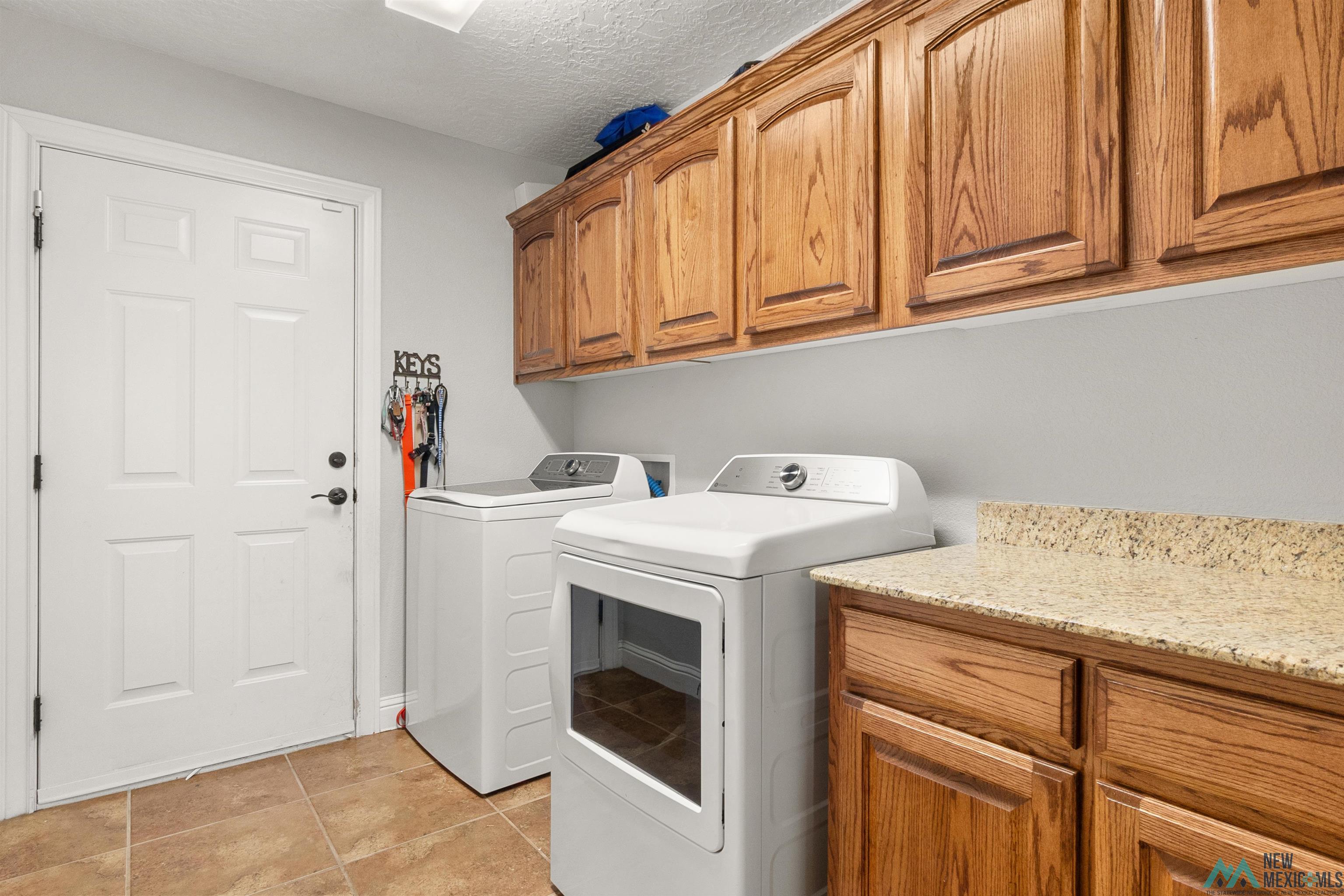 3913 Woodlark Road Clovis, NM 88101 - Photo 26 of 28 Dedicated utility area featuring warm wood cabinetry, a light-toned countertop, and durable tile flooring