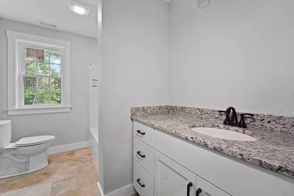 a bathroom with a granite countertop sink a toilet and a window