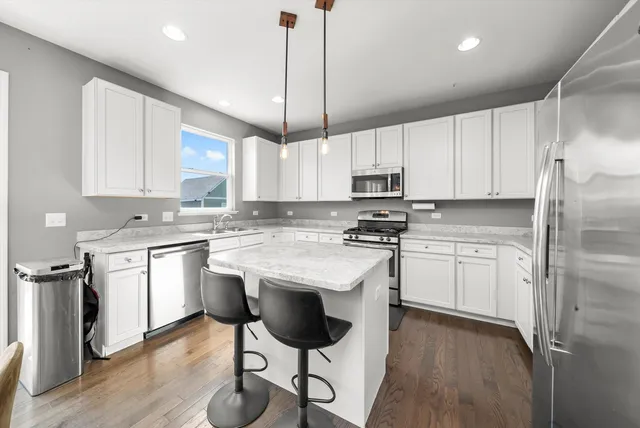 a kitchen with kitchen island granite countertop stainless steel appliances a stove a sink a refrigerator cabinets and chairs