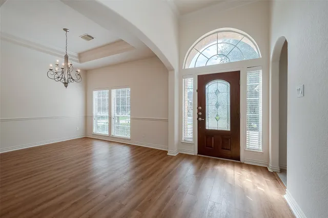 an empty room with wooden floor chandelier and a window