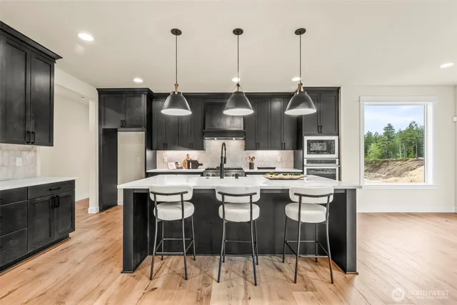 a kitchen with stainless steel appliances kitchen island granite countertop a stove a refrigerator a sink a dining table and chairs with wooden floor
