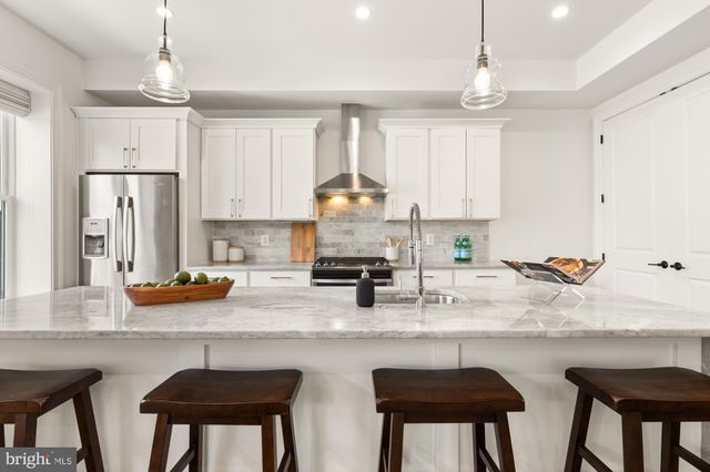 a kitchen with stainless steel appliances granite countertop a sink a stove a refrigerator a center island and chairs