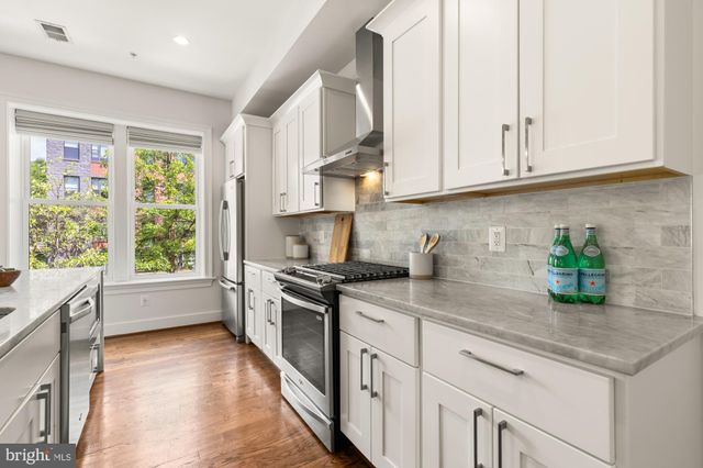 a kitchen with stainless steel appliances granite countertop a sink a stove and a white cabinets next to a window