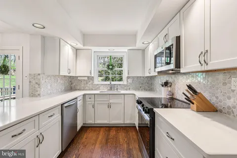 a kitchen with a sink dishwasher a stove and white cabinets with wooden floor