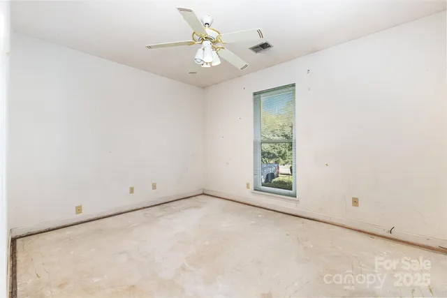 an empty room with a chandelier fan and windows