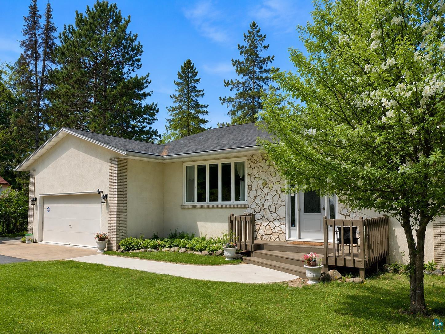3975 Long Lake Shores Road Eveleth, MN 55734 - Photo 4 of 84 Stucco and stone exterior featuring a two-car garage, a front entry deck, and a mature flowering tree