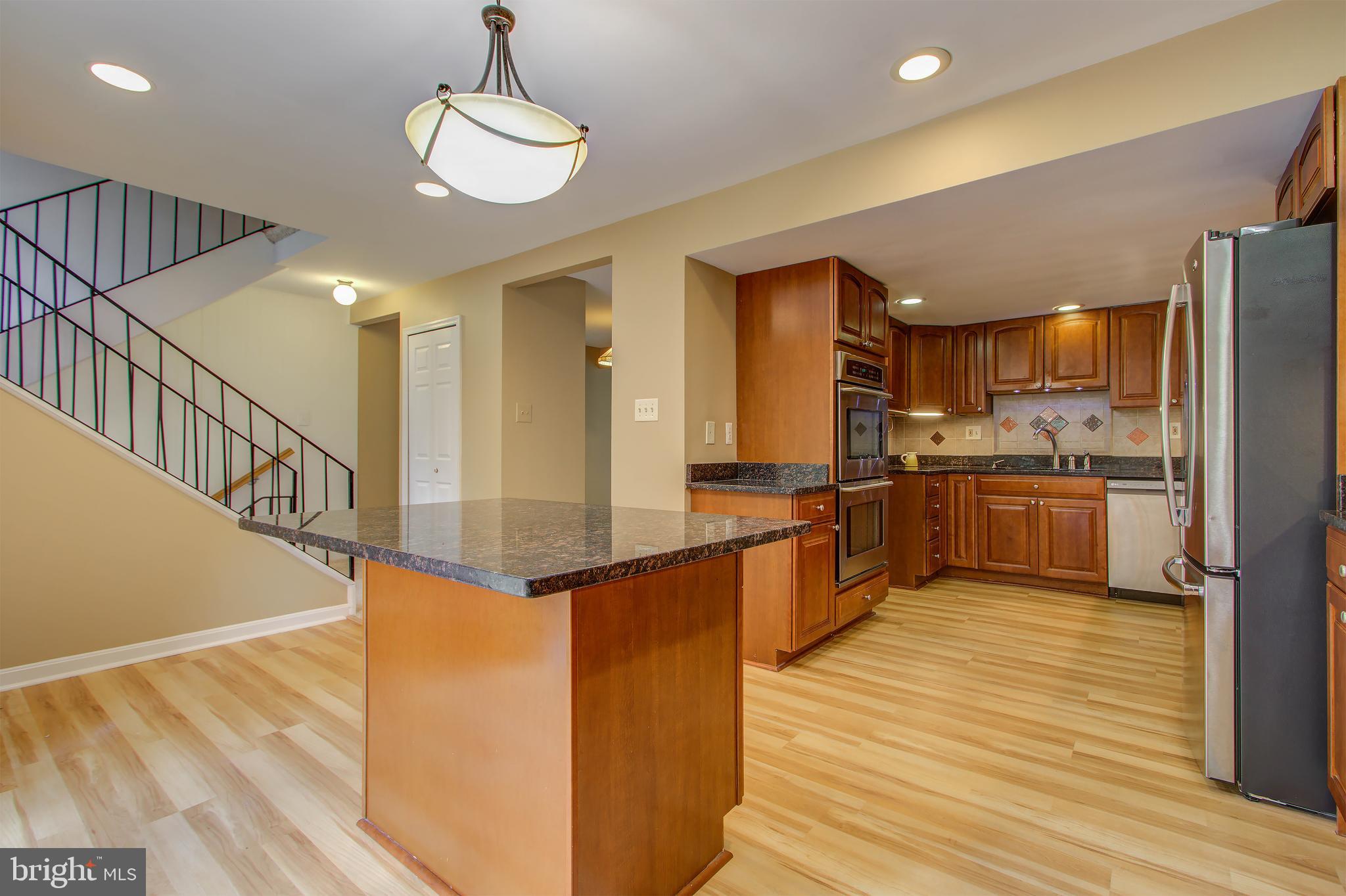 11024 Saffold Way Reston, VA 20190 - Photo 10 of 50 a kitchen with stainless steel appliances kitchen island granite countertop a refrigerator a stove and a wooden floors