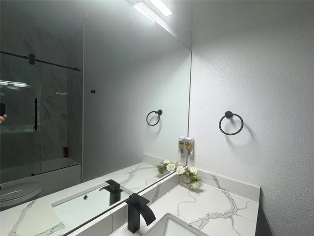 a bathroom with a granite countertop sink a mirror and shower