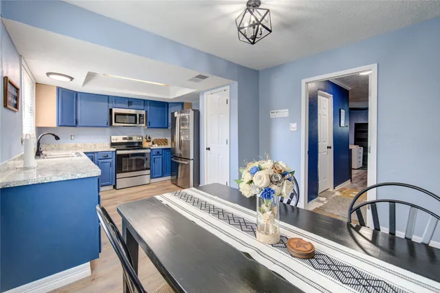 a kitchen with a refrigerator a stove a sink dishwasher a dining table and chairs with wooden floor