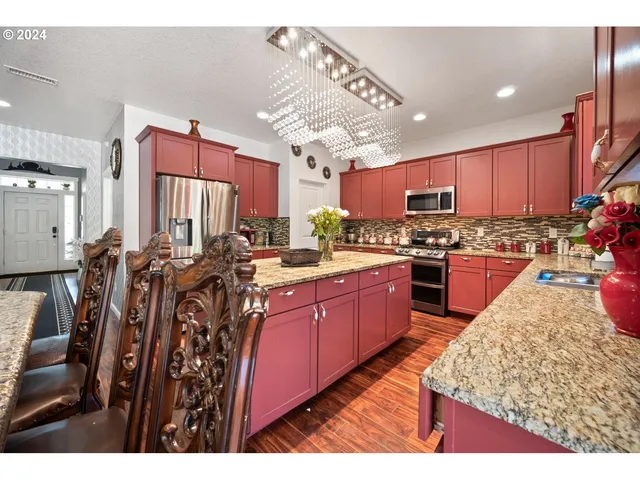 a kitchen with stainless steel appliances kitchen island granite countertop a stove a sink dishwasher and a refrigerator with wooden floor