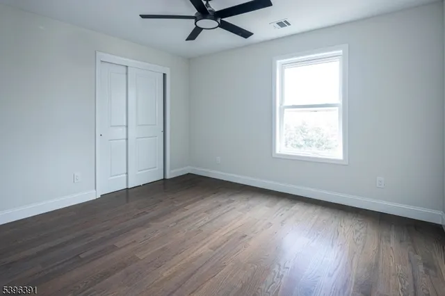 an empty room with wooden floor ceiling fan and windows