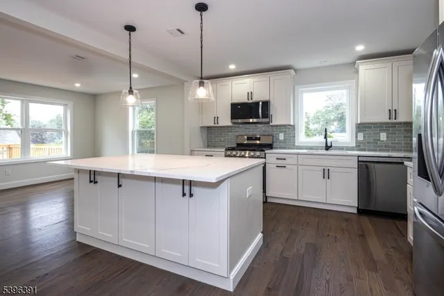 a kitchen with stainless steel appliances a sink a stove a microwave a center island and wooden floor