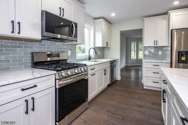 a kitchen with stainless steel appliances kitchen island granite countertop a stove top oven a sink dishwasher a refrigerator and cabinets with wooden floor