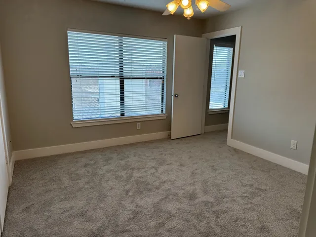 an empty room that has a window and a chandelier fan