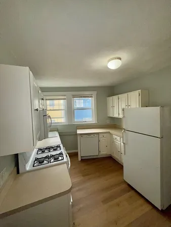 a kitchen with a white stove refrigerator and white cabinets with wooden floor