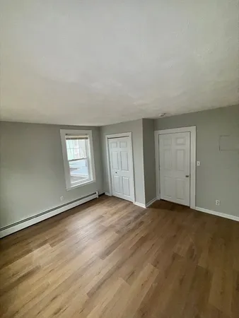 a view of an empty room with wooden floor and window