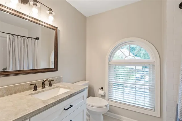 a bathroom with a granite countertop toilet a sink a mirror and a window