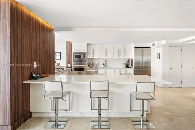a white kitchen with stainless steel appliances kitchen island granite countertop a refrigerator and cabinets