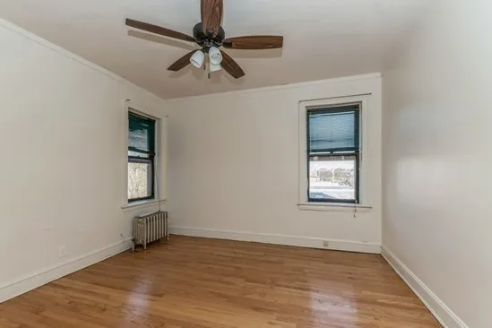 an empty room with wooden floor chandelier fan and windows