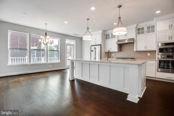 a kitchen with stainless steel appliances granite countertop a stove a sink dishwasher a refrigerator and a wooden floor