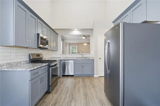 a kitchen with stainless steel appliances granite countertop white cabinets a refrigerator a sink a stove a microwave and wooden floors