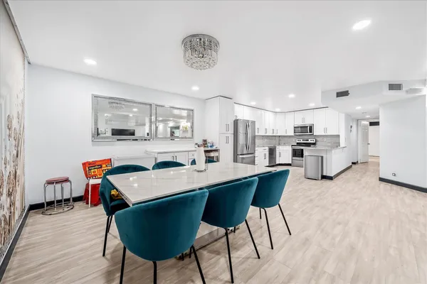 a room with stainless steel appliances kitchen island granite countertop a dining table chairs and a refrigerator