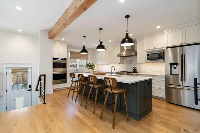 a kitchen with stainless steel appliances kitchen island granite countertop a dining table chairs sink and white cabinets