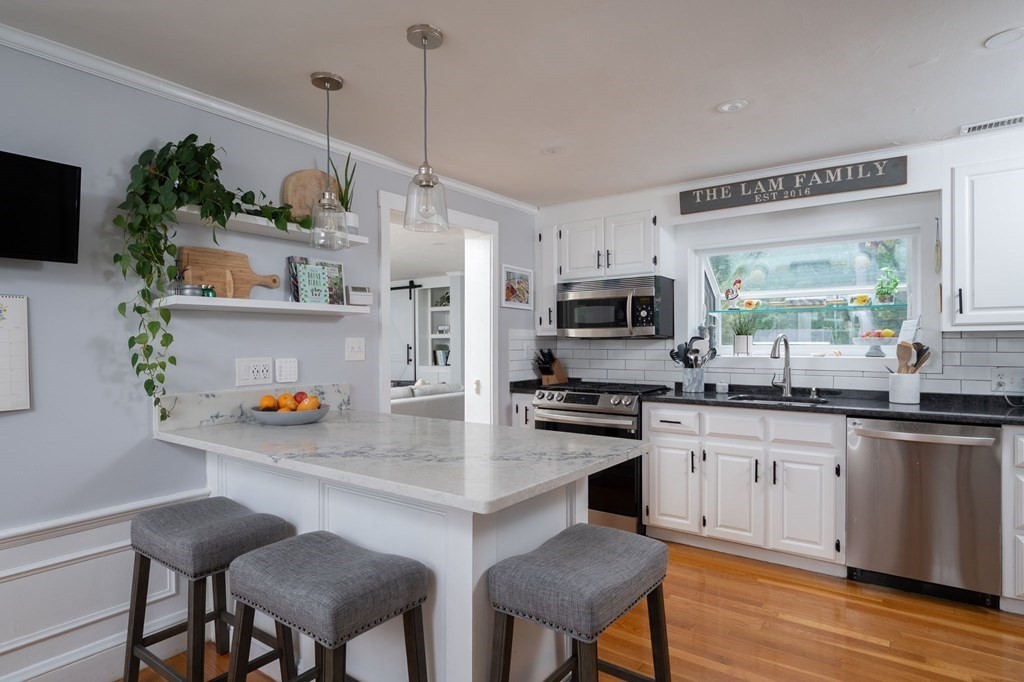 1054 Brook Road Milton, MA 02186 - Photo 4 of 23 a kitchen with stainless steel appliances granite countertop a stove a sink a refrigerator a microwave a dining table and chairs with wooden floor