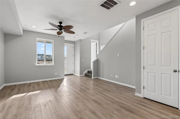 a view of an empty room with wooden floor and a ceiling fan