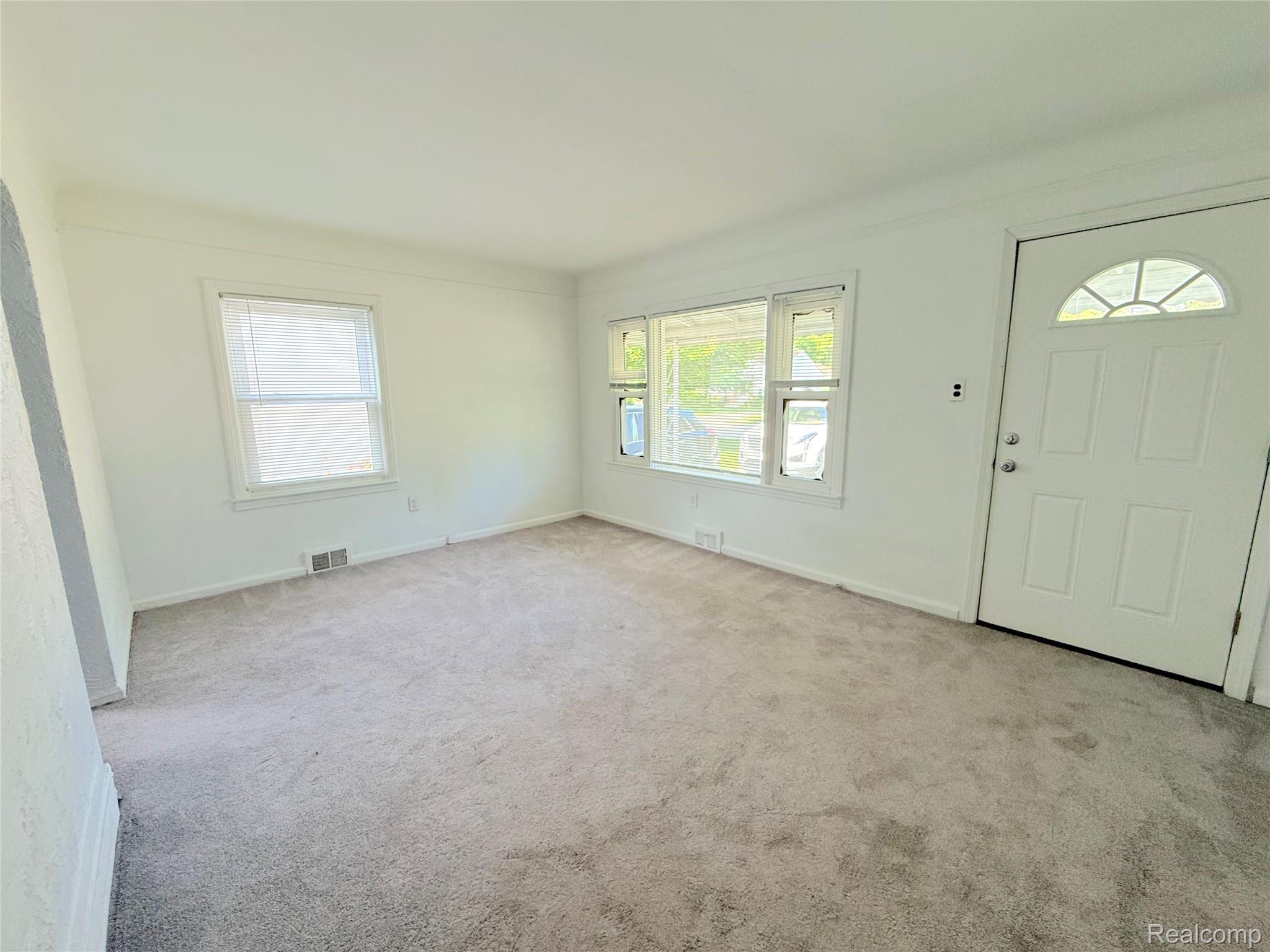 21212 Rensselaer Street Farmington, MI 48336 - Photo 2 of 11 Bright living space featuring light gray carpeting, multiple windows for ample natural light, and a paneled entry door with an arched transom window