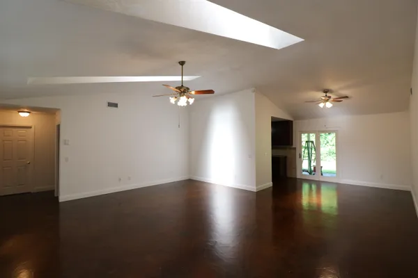 an empty room with wooden floor chandelier fan and windows