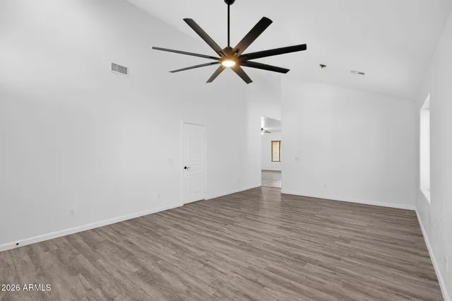 an empty room with wooden floor a ceiling fan and windows