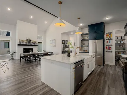 a kitchen with stainless steel appliances kitchen island granite countertop a stove top oven a refrigerator a dining table and chairs with wooden floor