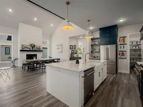 a kitchen with stainless steel appliances kitchen island granite countertop a stove top oven a refrigerator a dining table and chairs with wooden floor