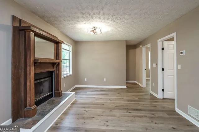 a view of an empty room with wooden floor fireplace and a window