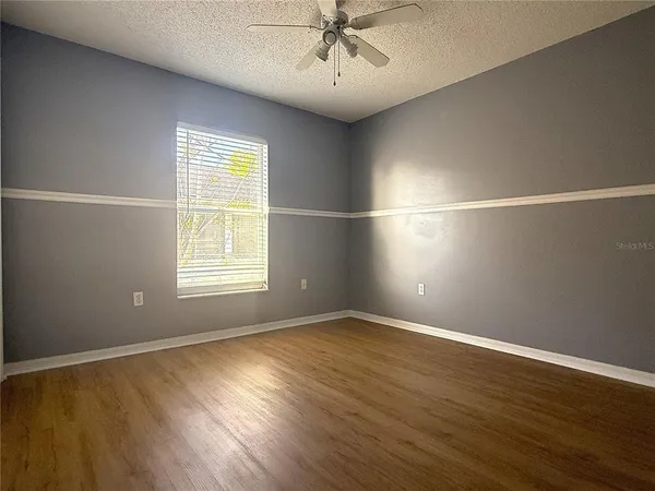 an empty room with wooden floor fan and windows