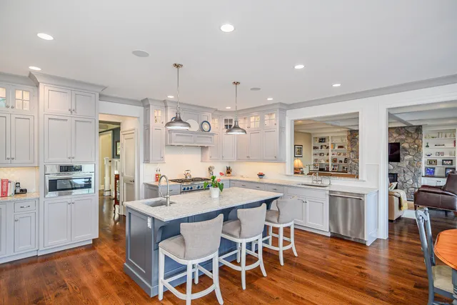 a kitchen with stainless steel appliances kitchen island granite countertop a stove a refrigerator a microwave oven a dining table and chairs with wooden floor