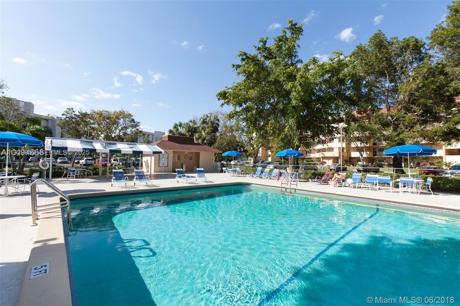 3821 Environ Boulevard, Unit 107 Lauderhill, FL 33319 - Photo 16 of 19 a swimming pool that has lawn chairs and a dining table under an umbrella