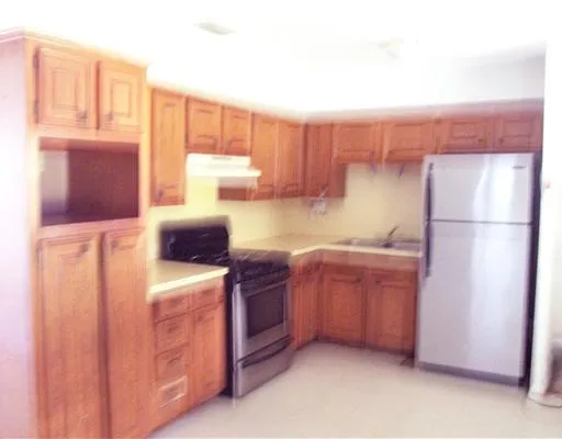 a kitchen with stainless steel appliances granite countertop a refrigerator a stove and a sink with wooden cabinets